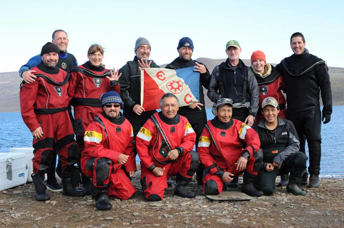 Dr. Martin Nweeia's team, Inuit hunters, and Fisheries and Oceans Canada members pose with the Explorer's Flag at Pond Inlet.