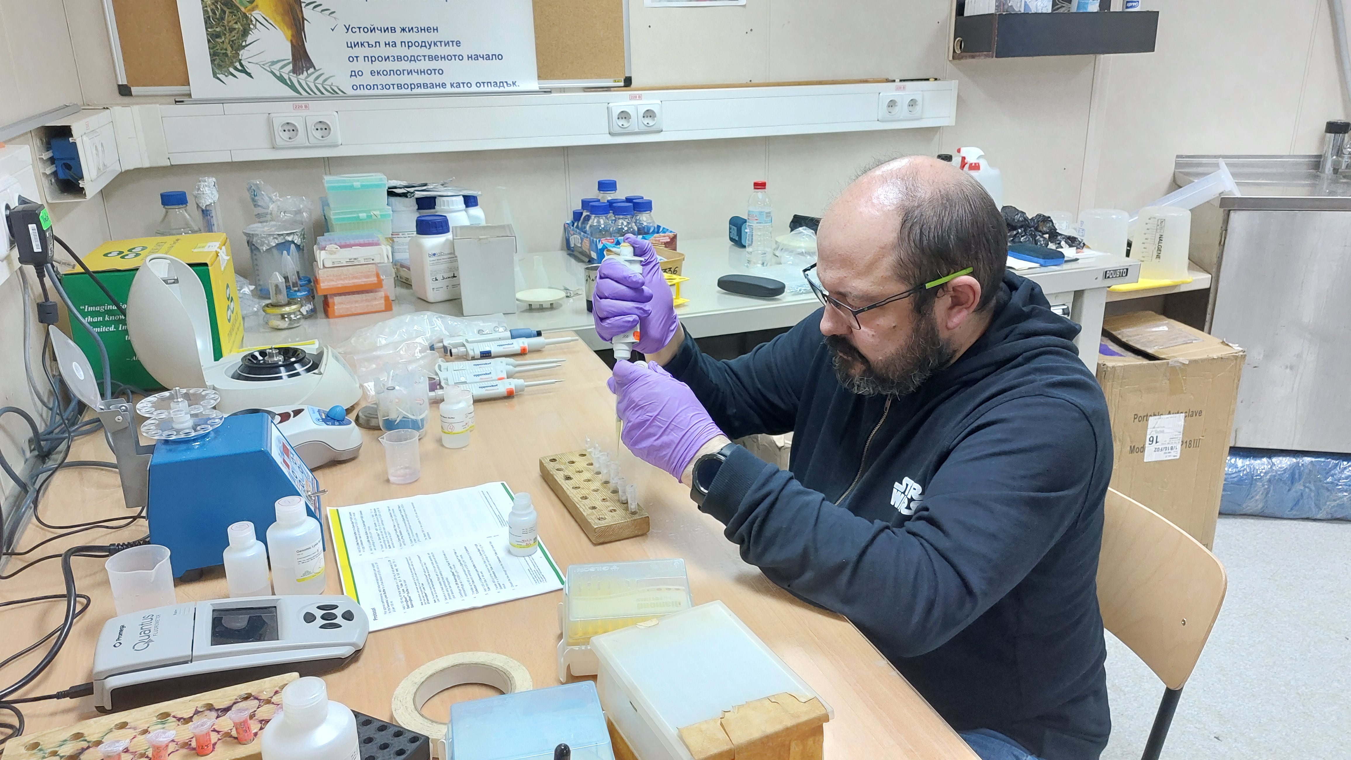 Scientist pipetting samples at a laboratory bench equipped with molecular biology equipment.