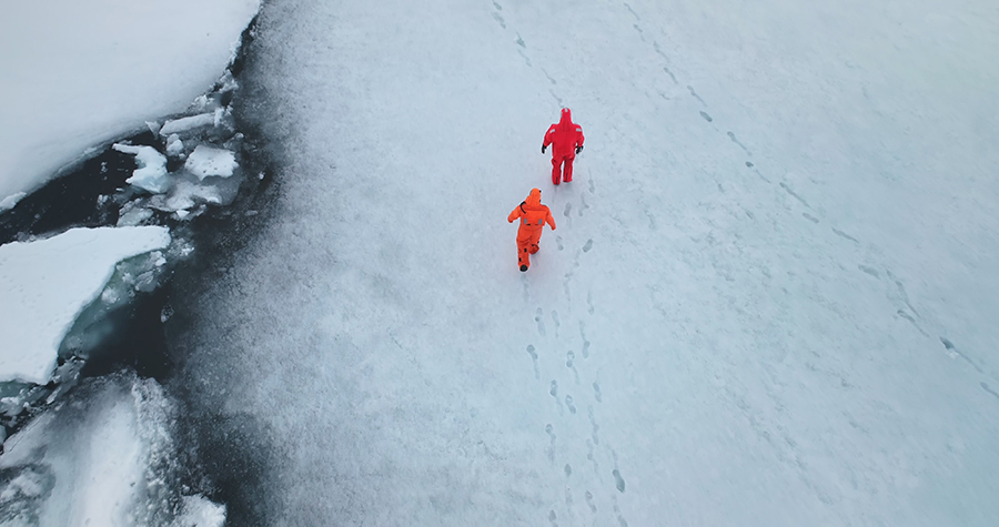 Two people in immersion suits walking in Antarctic ice.