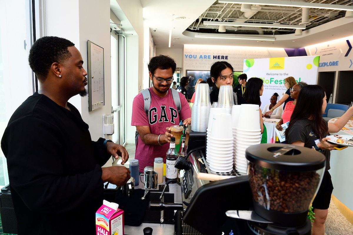 Attendees line up at a coffee station during the BioFestival event, with a barista preparing drinks and Zymo Research’s booth visible in the background.