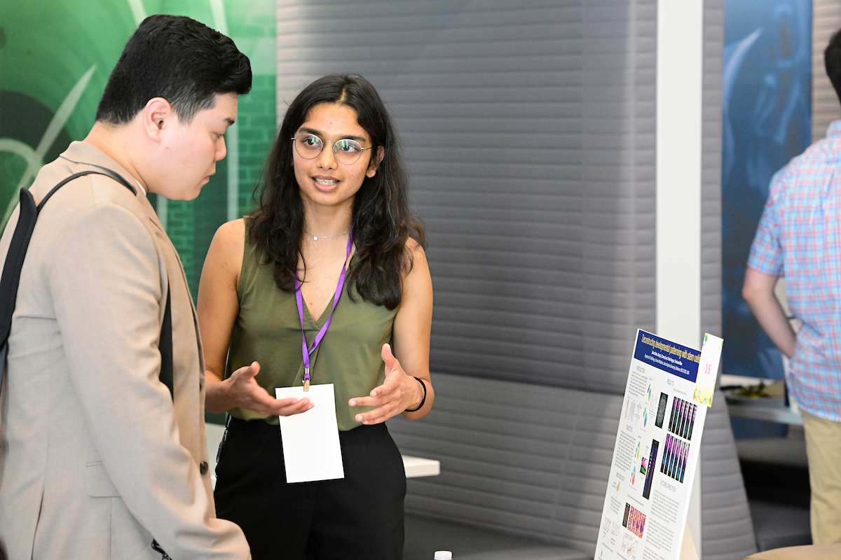 A student presents a scientific research poster to a judge during the BioFestival event, explaining her findings and discussing the displayed data.