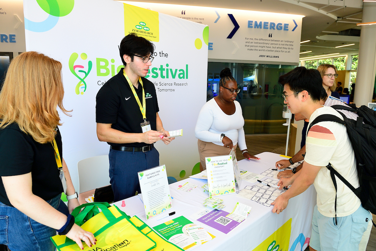 Zymo Research representatives engage with attendees at the BioFestival booth, handing out materials and explaining event activities.