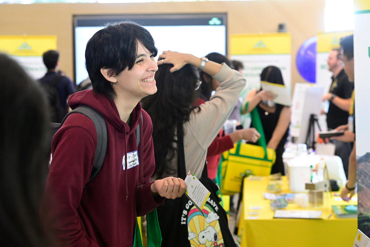 An attendee smiles and chats with others while exploring a Zymo Research booth at the BioFestival event.