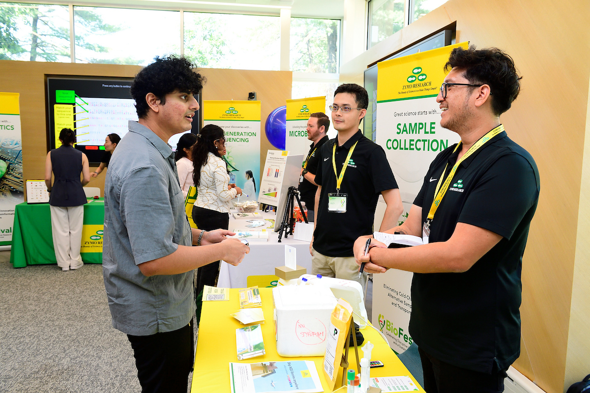 An attendee speaks with Zymo Research representatives at a booth displaying sample collection products during the BioFestival event.