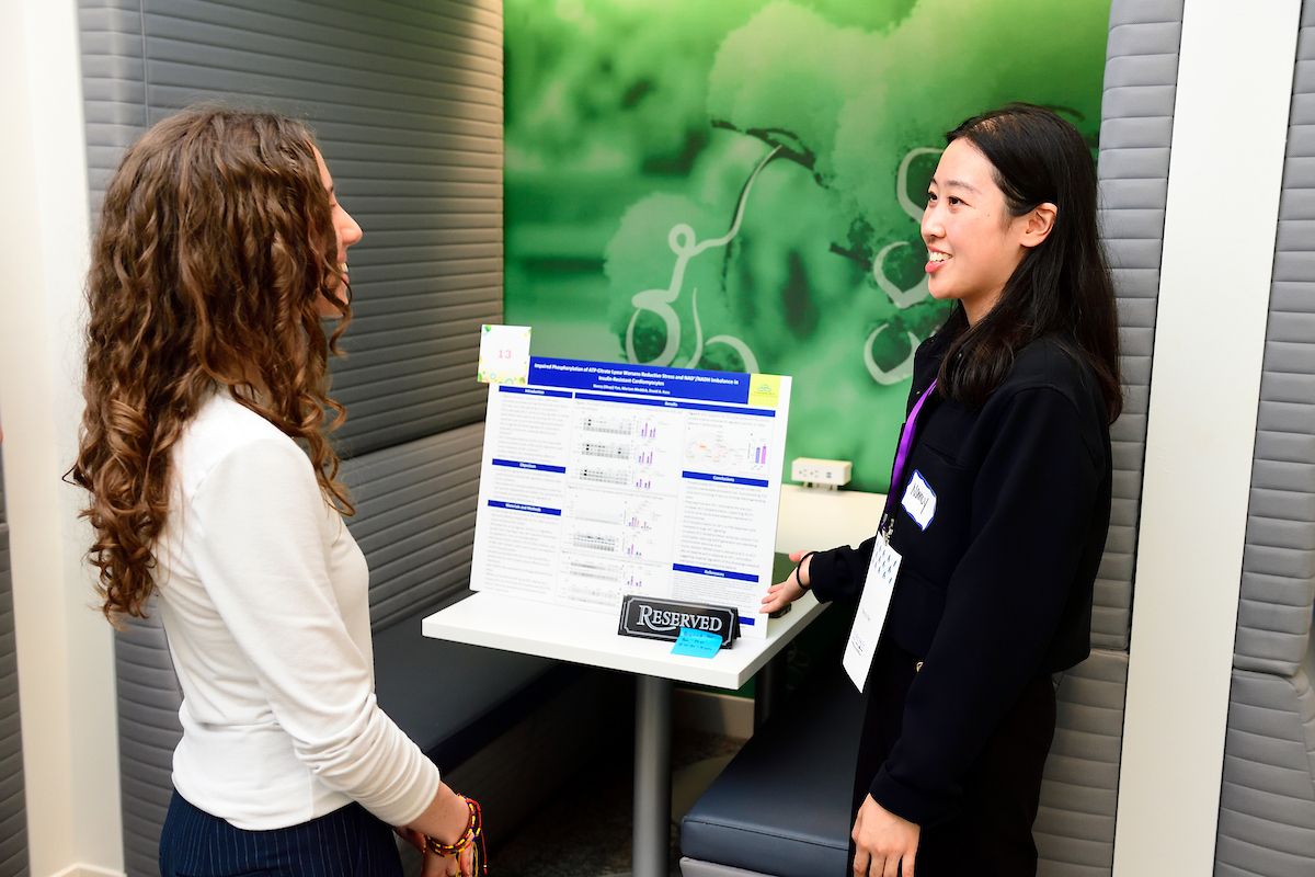 A student presents her scientific research poster to a judge during the BioFestival event, explaining data and findings in a discussion setting.