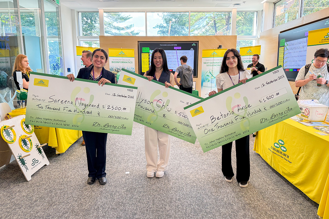 Three BioFestival grant award winners hold large ceremonial checks from Zymo Research, smiling and posing for a photo at the event.