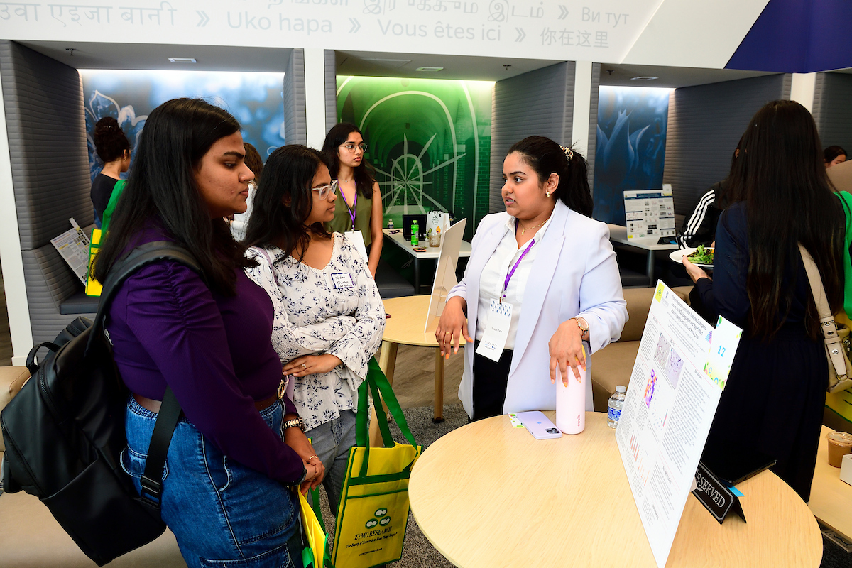 A student presents her scientific research poster to attendees during the BioFestival event, explaining her project and findings in a discussion.