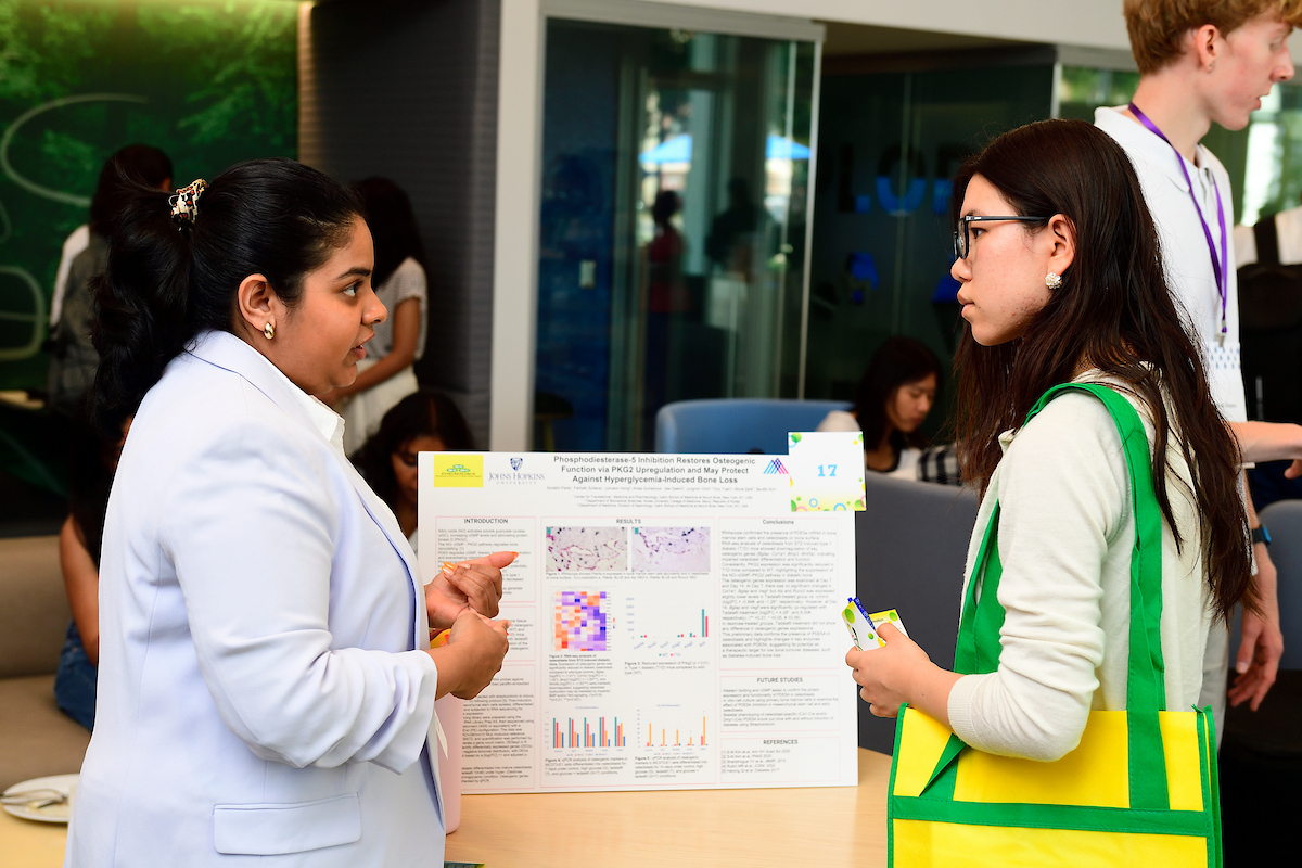 A student presents her scientific research poster to an attendee during the BioFestival event, discussing data and experimental results.