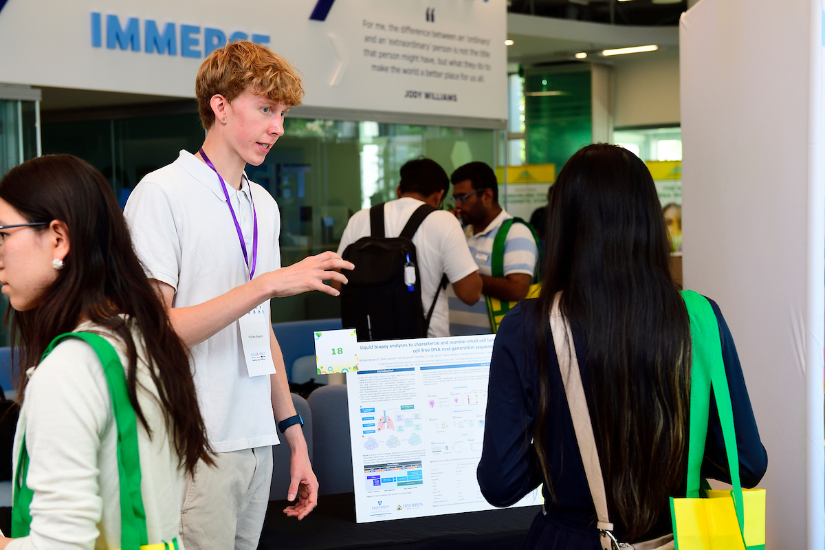 A student presents his scientific research poster to an attendee during the BioFestival event, explaining findings and answering questions.