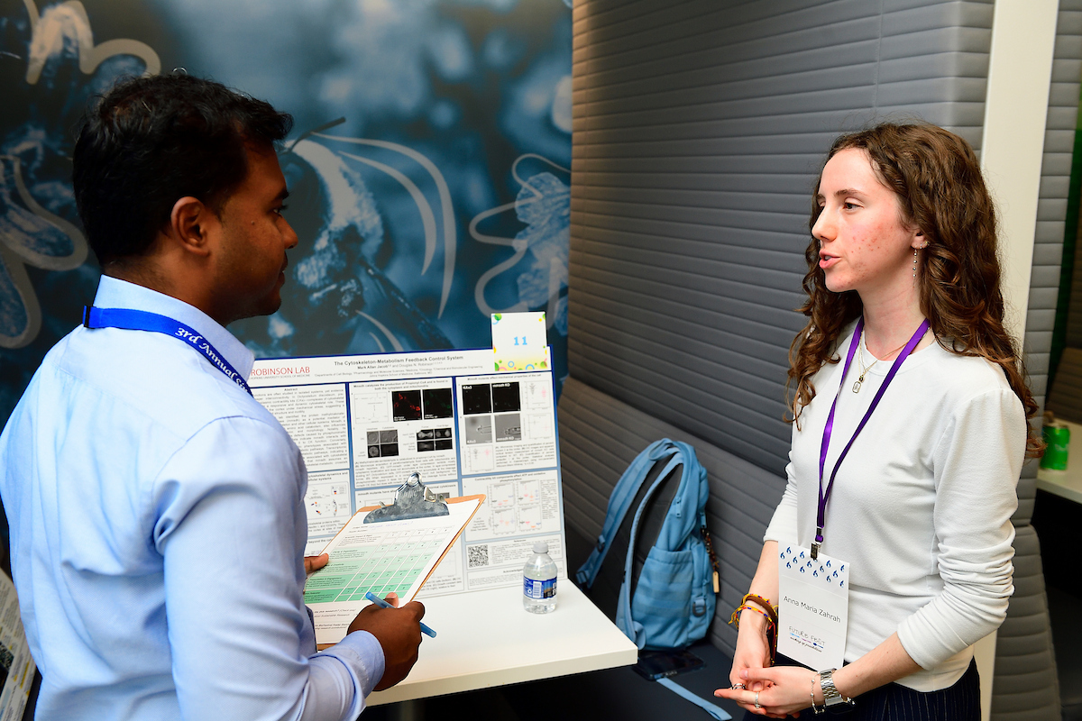A student presents her scientific research poster to a judge during the BioFestival event, discussing her findings and answering questions.