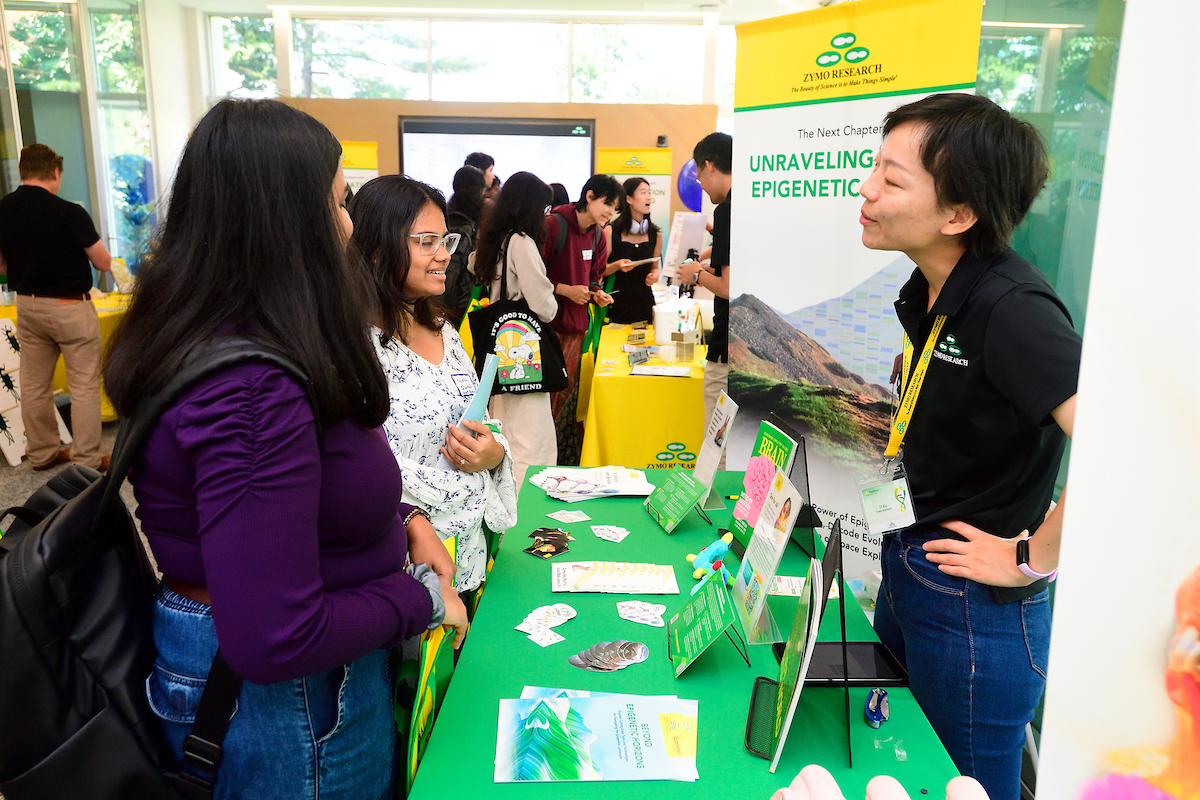 Attendees speak with a Zymo Research representative at a booth showcasing epigenetics and molecular biology displays during the BioFestival event.
