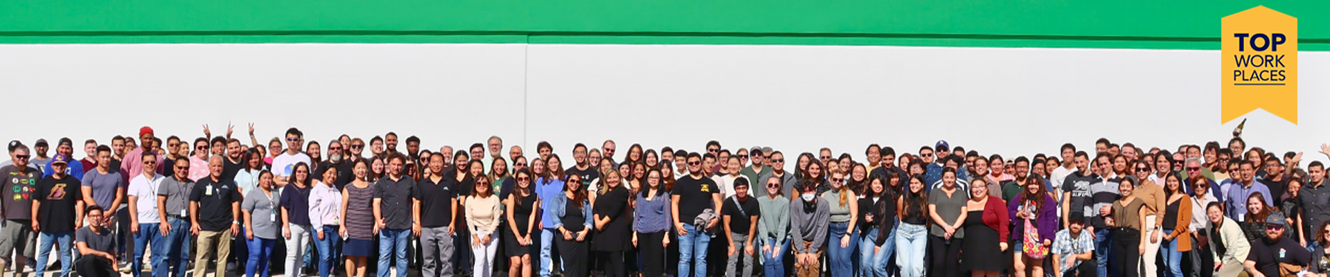 A big group of Zymo employees in front of a building, with a graphic badge that says Top Work Place on the top right of the image