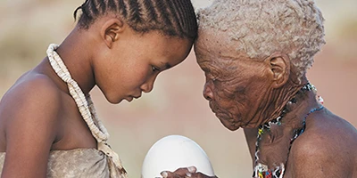 Indigenous bushman san girl given ostrich egg by elderly woman in Namibia.