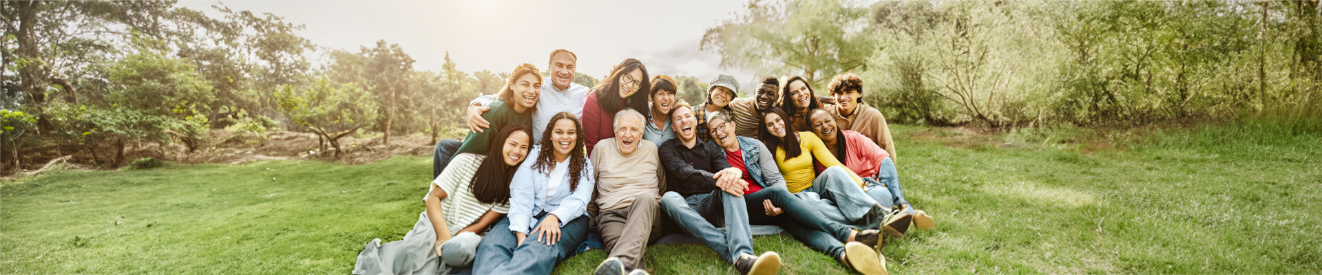 Banner image of a group of people sitting in a field, holding each other